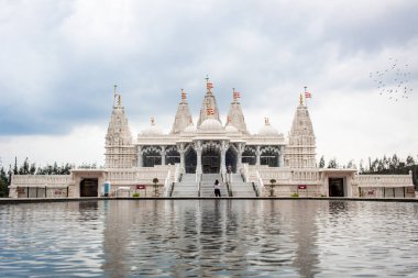 Ağaçlar ve suyla çevrili beyaz BAPS Shri Swaminarayan Mandir tapınağı. Fotoğraf bulutlu bir günde Houston Teksas 'ta çekildi.