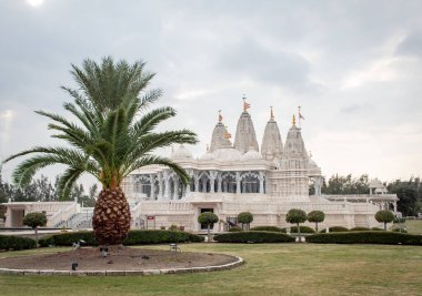 Ağaçlar ve suyla çevrili beyaz BAPS Shri Swaminarayan Mandir tapınağı. Fotoğraf bulutlu bir günde Houston Teksas 'ta çekildi.