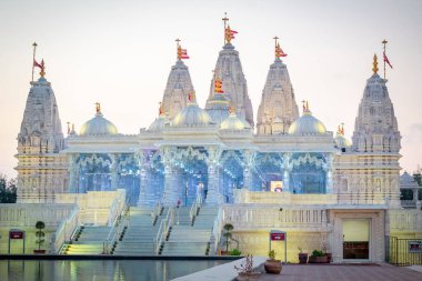 Sarı ışıklı BAPS Shri Swaminarayan Mandir, mor gün batımında suya karşı yansıdı. Fotoğraf Houston Teksas 'ta çekildi.