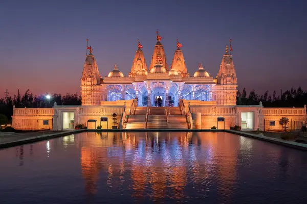Mor gün batımında, turuncu renkte aydınlatılmış BAPS Shri Swaminarayan Mandir suya karşı yansıdı. Fotoğraf Houston Teksas 'ta çekildi.
