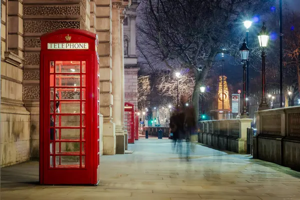Westminster 'da bir kaldırımda ışıklandırılmış kırmızı, eski Londra telefon kulübesi. Fotoğraf İngiltere 'de, Londra' da çekilmiştir.
