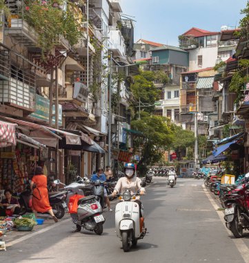 Hanoi Vietnam sokaklarında motosiklet süren bir kadın. Fotoğraf gündüz çekilmiş..