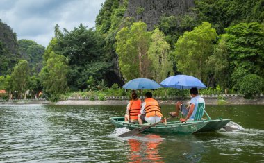 Tropik yemyeşil ormanlar ve dağlarla çevrili bir nehirde yüzen insanlar. Tam Coc Ninh Binh Vietnam 'da.
