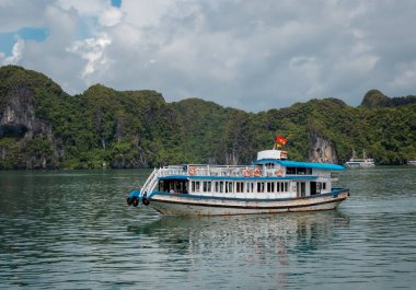 Vietnam 'daki Halong Körfezi' nde tropik ada kireçtaşı dağları, su ve tekne manzarası.