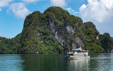 Vietnam 'daki Halong Körfezi' nde tropik ada kireçtaşı dağları, su ve tekne manzarası.