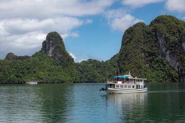 Vietnam 'daki Halong Körfezi' nde tropik ada kireçtaşı dağları, su ve tekne manzarası.