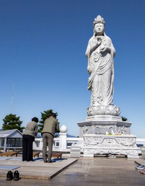 İnsanlar ayakta duran dev bir Buda heykeline dua ediyor ve ona tapıyorlar. Fotoğraf Güney Kore, Sokcho 'daki Naksansa Budist Tapınağı' nda çekildi.