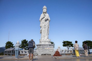 İnsanlar ayakta duran dev bir Buda heykeline dua ediyor ve ona tapıyorlar. Fotoğraf Güney Kore, Sokcho 'daki Naksansa Budist Tapınağı' nda çekildi.