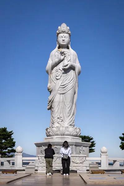 İnsanlar ayakta duran dev bir Buda heykeline dua ediyor ve ona tapıyorlar. Fotoğraf Güney Kore, Sokcho 'daki Naksansa Budist Tapınağı' nda çekildi.