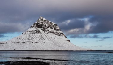 İzlanda 'nın Snfellsnes yarımadasında yer alan Kirkjufell Dağı karla kaplıydı. Fotoğraf, kışın bulutlu bir günde çekildi.