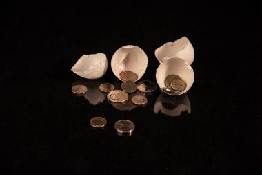 Broken eggshells with small change on black background. Conceptual image regarding financial issues.   clipart