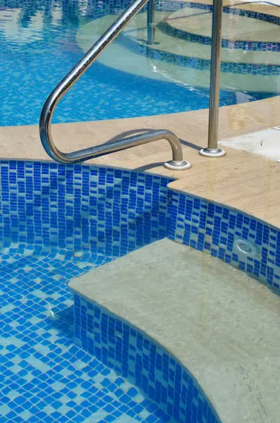 Mozaik fayansların mimari ayrıntıları ve mavi yüzme havuzunun su yansıtmalı mermer basamakları.