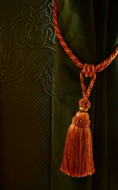 Turuncu tasma kadife perdeleri tutuyor.