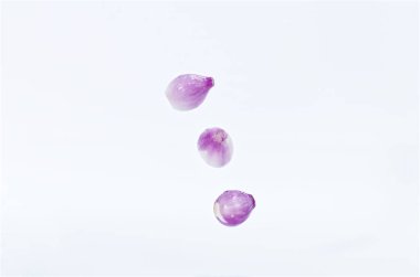 Canlı mor arpacık soğanlarından oluşan bir üçlü beyaz bir arkaplan üzerinde havada yüzüyor, tazeliklerini vurguluyor..