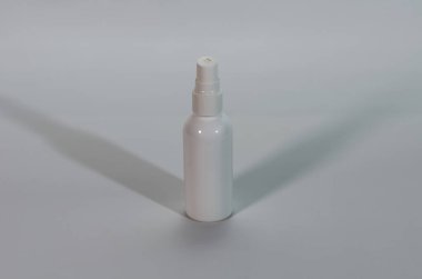 Minimalist tarafsız bir arkaplana karşı dimdik duran temiz, beyaz bir plastik sprey şişesi ince bir gölge oluşturur..