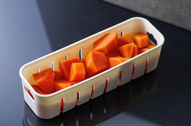 Sulu ve canlı papaya küpleri küçük beyaz bir kabın içinde düzgünce dizilmiş.