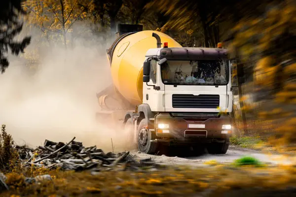 Sarı bir beton karıştırıcı kamyon toprak yolda hızla ilerliyor, toz kaldırıyor. Vahşi ve gelişmemiş bir alanda hızla ilerleyen bir inşaat kamyonu. Ağır inşaat ekipmanları ve ağırlığı. Beton zor bir konuma taşınıyor
