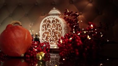 Evde Noel süsleri. Beyaz bir kanepede beyaz bir fener, kırmızı böğürtlen ve turuncu bir hokkaido kabağı. Hepsi narin bir şekilde Noel ışıklarına sarılmış. Evde Noel öncesi konforu. Geçmişe dönük iç tasarım. Dönüştürmeli kamera sürücüsü