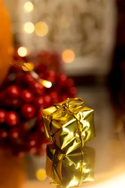 Noel hediyesi, Noel süsleri ve ışıklarının arasında altın iplikli küçük bir paket. Arka planda kırmızı bir dut var. Noel süsleri, karşılıklı hafıza ve nezaketin jestleri. Metin için alanı olan dikey çerçeve.