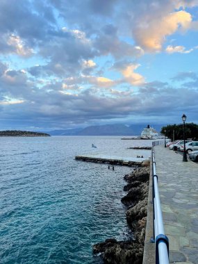 Yunanistan 'ın Girit adasında kıyıya yanaşmış bir yolcu gemisinin bulunduğu pitoresk bir sahil geçidi. Sakin turkuaz sular ve dramatik bir gökyüzü sakin ve manzaralı bir deniz havası yaratır.