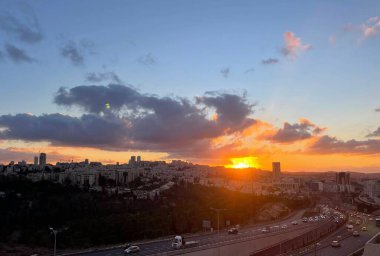 Kudüs 'ün üzerinde çarpıcı bir günbatımı. Şehrin panoramik manzarası ve canlı bulutlar. Doğal güzellik ve kentsel mimarinin karışımı, seyahat, kültür ve manzara temaları için ideal, sakin ve büyüleyici bir akşam atmosferi yaratır.