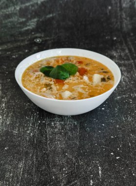 Siyah arka planda beyaz tabakta balık çorbası, mutfak havlusu, domates. 