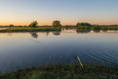 Ağaçlarla dolu bir çayırın ortasında küçük bir göl ve güzel bir günbatımı.