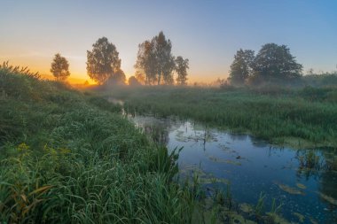 Sabah manzarası. Önünde bir göl ve bir nehir var..