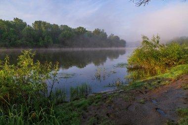 Bir gölün kıyısında gün doğumu. Nehrin üzerinde sabah sisi.
