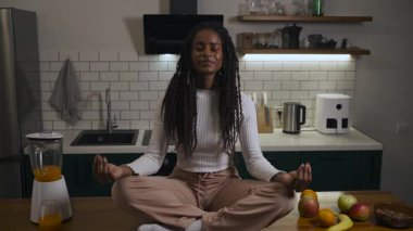 Sakin Afrikalı Amerikalı kadın evdeki modern bir mutfakta masada meditasyon yapıyor. Yüksek kalite 4k görüntü