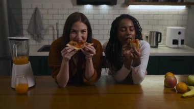 Evdeki modern bir mutfakta lezzetli pizzanın tadını çıkaran iki çok ırklı kadının portresi. Yüksek kalite 4k görüntü