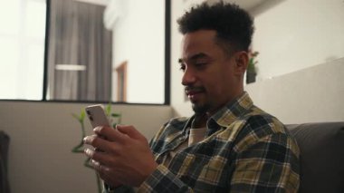 Mutlu Amerikalı adam evde oturuyor, telefonda yazıyor ve gülüyor. Yüksek kalite 4k görüntü