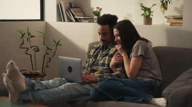 Mutlu uluslararası çift evlerindeki oturma odalarında kanepede oturuyor ve dizüstü bilgisayarlarıyla bir gezi ayarlıyorlar. Yüksek kalite 4k görüntü
