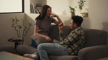 Mutlu çok ırklı çift modern bir oturma odasında kanepede oturuyor konuşuyor ve gülüyor sonra da yastık savaşına gülücükle başlıyorlar. Yüksek kalite 4k görüntü