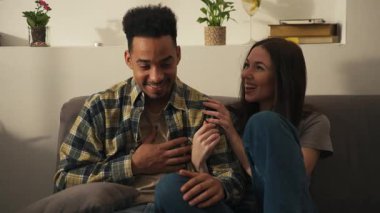 Genç, çok kültürlü bir çift evdeki modern bir oturma odasında el ele tutuşup kahkahalar atıyorlar. Yüksek kalite 4k görüntü