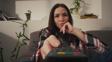 Sıkıcı kadın uzaktan kumandayla kanal değiştirip ilginç bir şey bulmaya çalışıyor. Yüksek kalite 4k görüntü