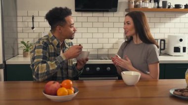 Çok kültürlü bir çift mutfakta kahvaltı yapıyor. Kadın konuşurken erkek mısır gevreği yer ve sabah sohbeti sırasında gülümser. Yüksek kalite 4k görüntü