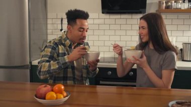 Mutfak masasında birlikte kahvaltı eden çok kültürlü bir çift. Mısır gevreğini sütle yerler, gülümserler, konuşurlar ve sıcak ve aydınlık bir sabah atmosferinin tadını çıkarırlar. Yüksek kalite 4k görüntü