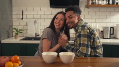 Mutfak masasında oturmuş birbirine eşlik eden çok kültürlü bir çift. Gülümsüyorlar, konuşuyorlar, el ele tutuşuyorlar, sonra bir kase mısır gevreği alıp birlikte kahvaltı etmeye başlıyorlar. Yüksek kalite 4k görüntü