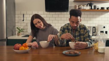Mutfak masasında kahvaltı yapan çok kültürlü bir çift. Kurabiyeleri süte bandırıp yiyorlar. Birlikte neşeli ve hafif bir sabahın tadını çıkarıyorlar. Yüksek kalite 4k görüntü