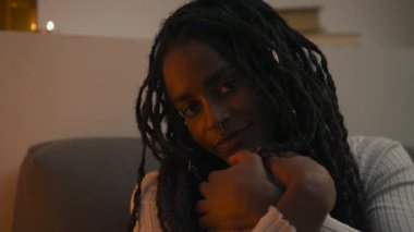 Genç bir Afro-Amerikan kadının yakından çekilmiş portresi aşağı bakıyor, sonra sakin ve samimi bir ortamda nazikçe gülümseyerek kameraya bakıyor. Yüksek kalite 4k görüntü