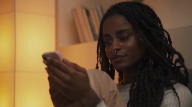 Akıllı telefon tutan genç bir Afro-Amerikan kadının yakın plan portresi ve hafif bir gülümsemeyle ekrana bakıyor. Yüksek kalite 4k görüntü