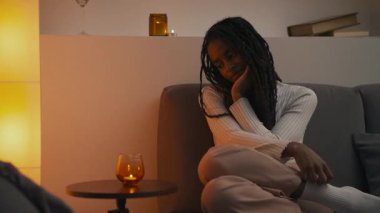 Genç bir Afrikalı Amerikalı kadın akşamları bir kanepede oturur, rüya gibi bir kadınla masanın üzerindeki mumu seyreder. Yüksek kalite 4k görüntü