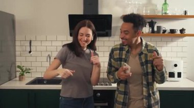 Mutfakta dans eden çok kültürlü bir çift birlikte müzik dinlerken her biri salata malzemesi olarak bir kulaklık takıyor masaya oturuyor. Yüksek kalite 4k görüntü