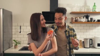 Mutfakta çok kültürlü bir çift var. Kamera yakın plandan geniş açıya geçerken kadın dilimlenmiş domatesin tadını alırken erkek dans edip ona arkadan sarılıyor. Yüksek kalite 4k görüntü