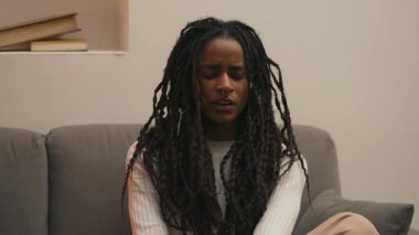 Yorgun Afrika kökenli Amerikalı kadın, kamera hafifçe hareket ederken kanepe yastığına yaslanmadan önce esniyor ve esniyor. Yüksek kalite 4k görüntü