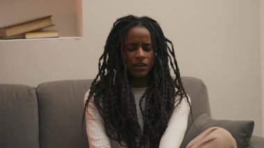 Kanepe yastığının üzerine yavaşça çökmeden önce esneyen ve gerinen Afrikalı Amerikalı bir kadın. Kamera hareketini takip etmek için hafifçe eğiliyor. Yüksek kalite 4k görüntü