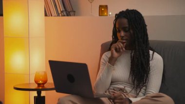 Geceleri dizüstü bilgisayarda çalışan Afrikalı Amerikalı bir kadın yorgun bir gülümsemeyle esniyor ve kapatıyordu. Sonra kanepeye kıvrılıyor ve sıcak ev atmosferinde bir mumu seyrediyordu. Yüksek kalite 4k görüntü