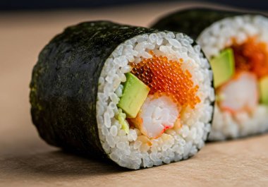 Avokado, karides ve yumurtayla dolu iki suşi rulosu yakın plan.