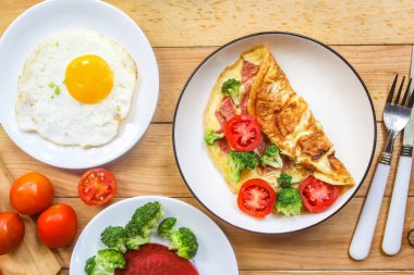 Kahvaltı menüsü olarak ahşap bir masada omlet, kızarmış yumurta ve sebze.